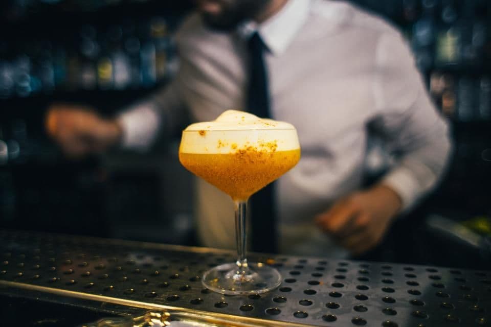 A bartender finishing a drink at a dark bar counter
